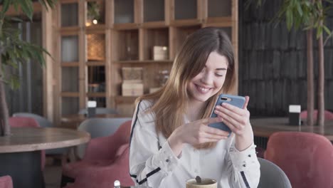 hermosa joven está sentada en un café y revisando sus mensajes en un teléfono