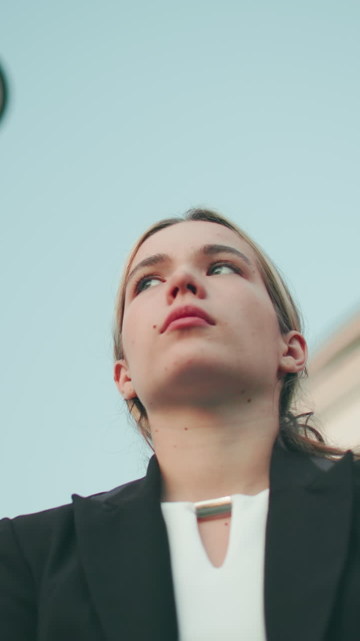Worried woman in professional outfit looks tired and lost in thought with iron railing behind her and modern glass building in background