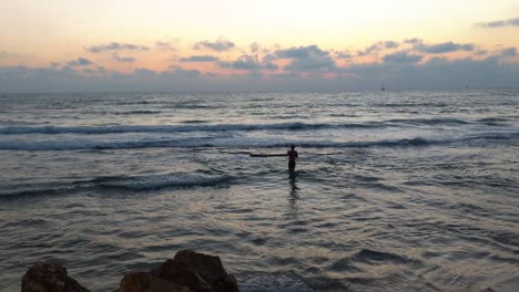 a fisherman walks in the sea, on the beach of tel aviv.the beach at sunset, waves breaking on the beachship sails deep into the sea, orange-colored sunset,tel aviv beach