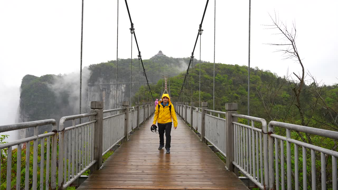 hombre con impermeable amarillo cruzando el puente colgante en la montaña tianmen en un día de niebla, china