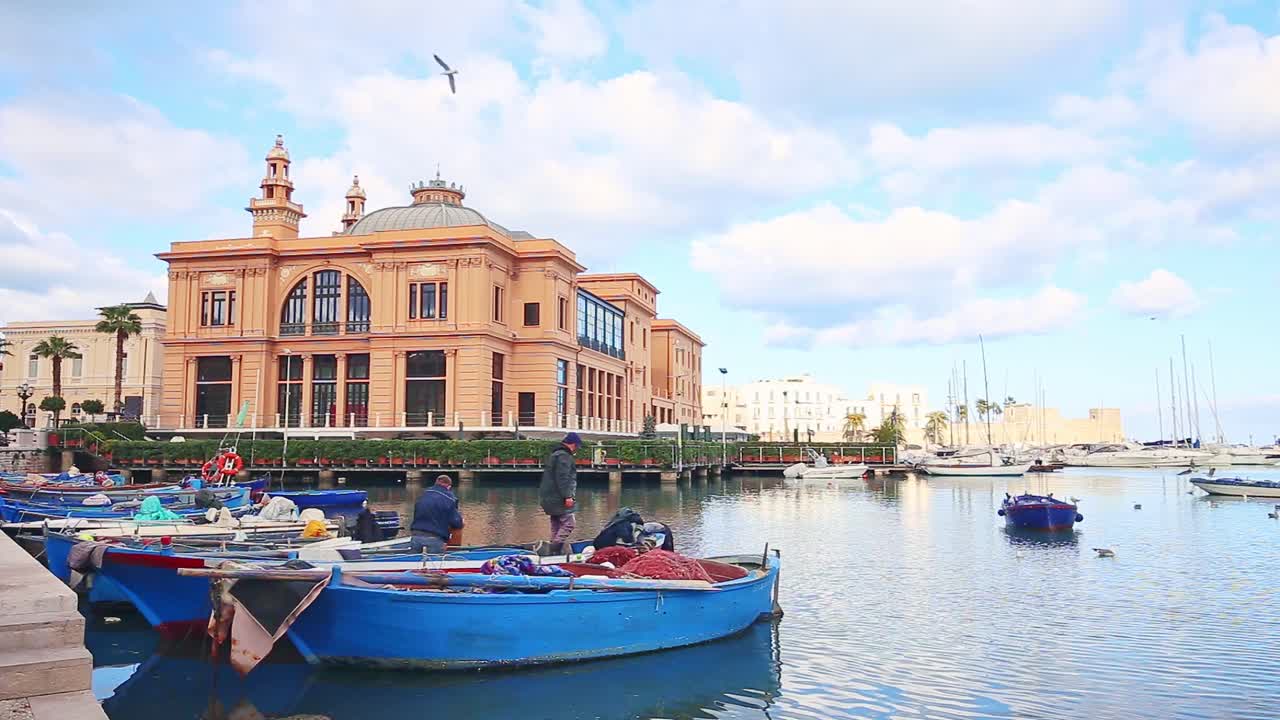 Fishermen preparing boats in Porto Vecchio old pier, seagulls flying, Margherita Theatre and Fortress in background, Bari, Italy