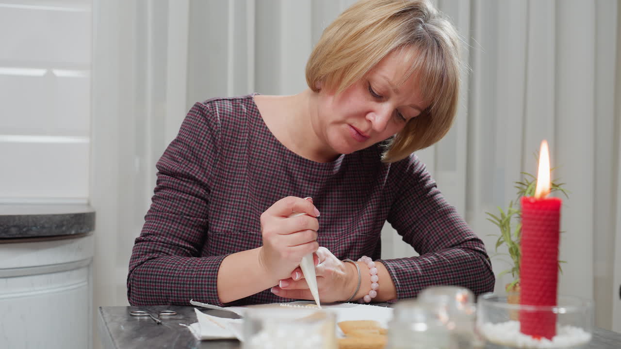 은 불, 가위, 식물로 둘러싸인 아이싱으로 쿠키를 장식하는 젊은 여성, 아한 부에서, 쿠키에 파이핑 봉투로 글러싱을 적용하는 손에 초점을 맞추십시오