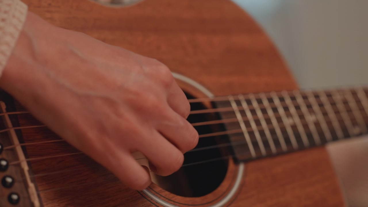 Tocando violão acústico em um ambiente interno aconchegante. Dedilhado delicado no violão sob iluminação interna suave. Batendo as cordas do violão acústico com trabalho detalhado no braço durante uma prática íntima em ambiente interno