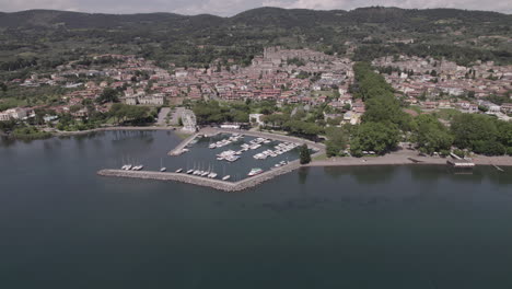 drone disparado volando sobre el lago bolsena en italia viniendo del agua a la antigua ciudad medieval con un castillo y edificios antiguos en la colina y un pequeño puerto en un día soleado