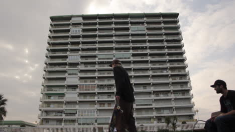 a skater stands in front of a towering apartment block at dusk, blending youth, solitude, and the quiet weight of concrete city life