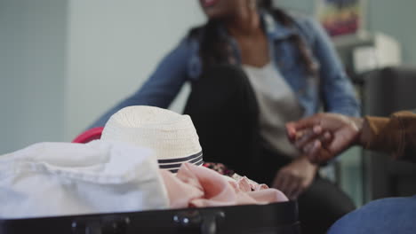 multinational friends take hat and swimsuit closing suitcase