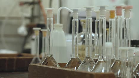 tilt down to a close up shot of volumetric flasks in a wooden box, which has clear solution in them