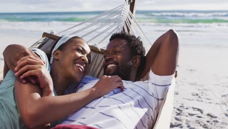 african american couple lying together on a hammock at the beach