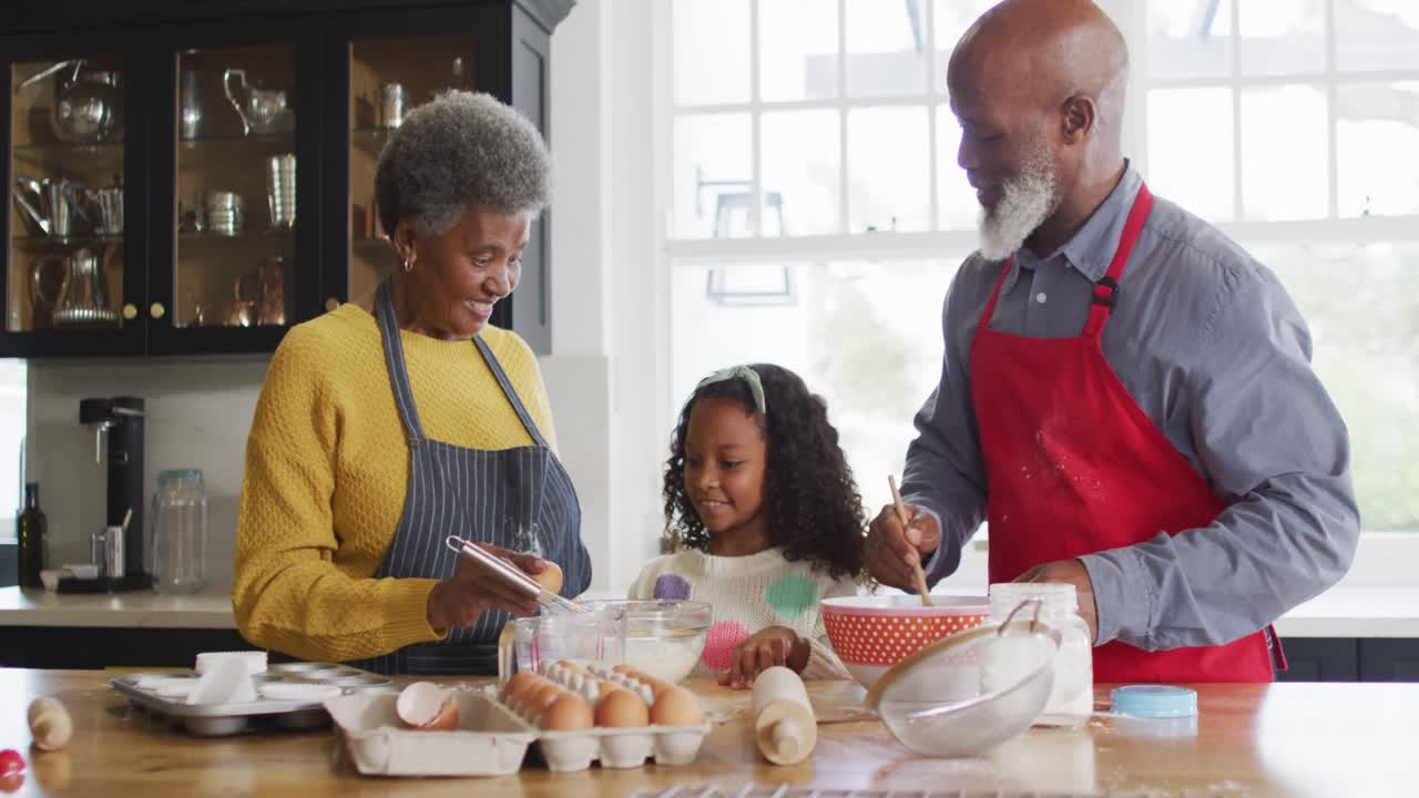 Video of happy african american granddaughter cooking with grandparents in kitchen
