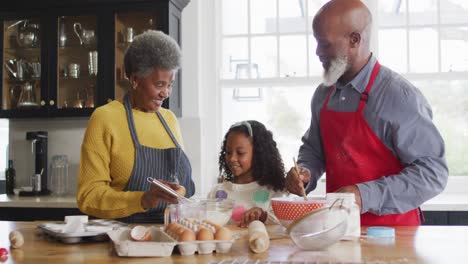 video of happy african american granddaughter cooking with grandparents in kitchen