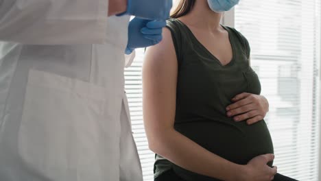 doctor applying sticking plaster  on arm of pregnant caucasian woman right after vaccination.