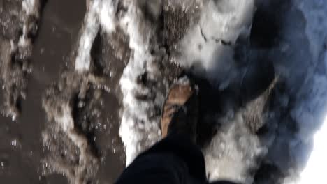 stiefelfüße laufen durch schmutzigen schnee und matsch auf einer stadtstraße