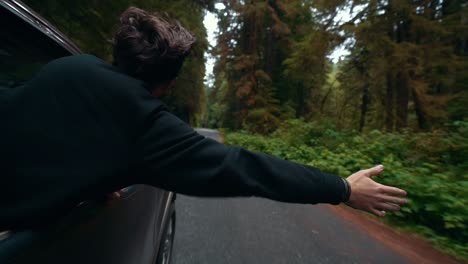 Young-male-with-his-head-out-the-window-on-a-forrest-road