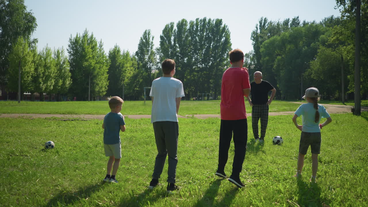 할아버지는 손자손녀들을 야외 스포츠 활동으로 이끌고, 아이들은 허리에 손을 고 서서 점프를 준비하고, 잔디에서 이 나는 날을 즐기고 있습니다.