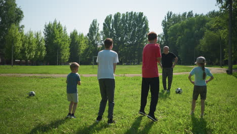 un abuelo conduce a sus nietos en una actividad deportiva al aire libre, los niños se paran con las manos en la cintura, preparándose para saltar, mientras disfrutan de un día soleado en un campo cubierto de hierba