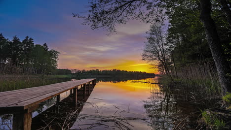 Hyperlapse-shot-of-wooden-jetty-and-branches-swimming-on-lake-surface-during-sunset-time-in-wilderness