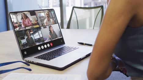 African-american-woman-using-laptop-for-video-call,-with-diverse-business-colleagues-on-screen