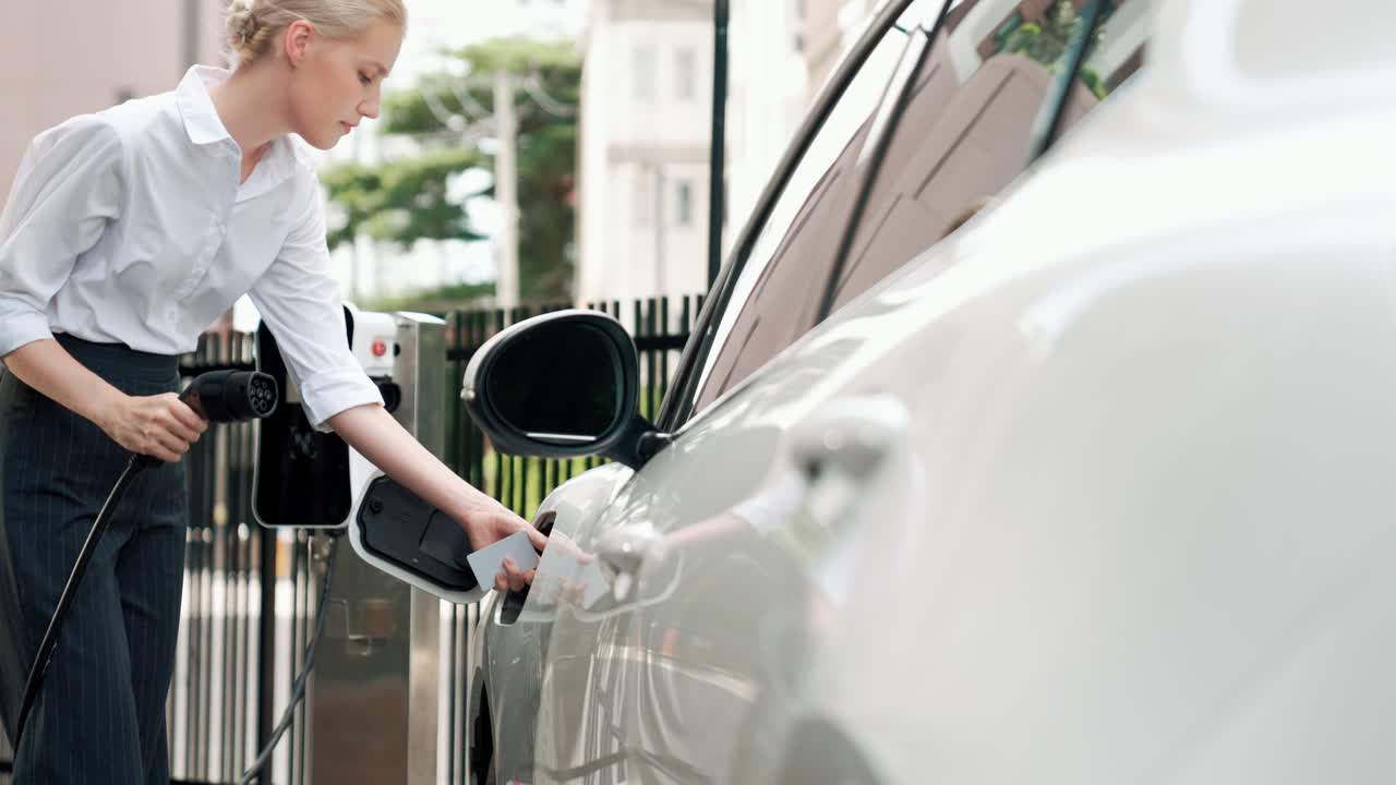 прогрессивная бизнесменка подключает зарядный разъем от зарядной станции к своему автомобилю.