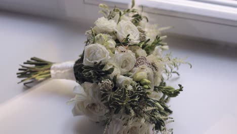 wedding golden rings lie on beautiful wedding white rose flowers bouquet on white window sill