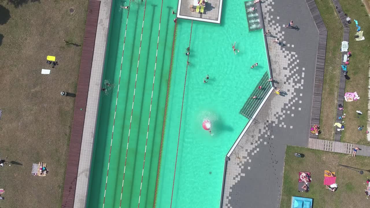 사람들이 물에서 즐거운 시간을 보내고 담요 위에 누워 있는 수영장의 최고 공중 전망 4k