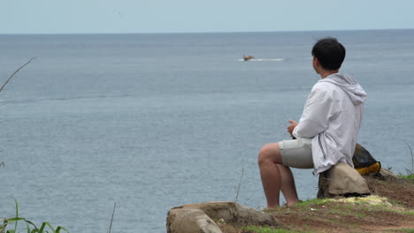 young man contemplating sits near seacoast. static shot