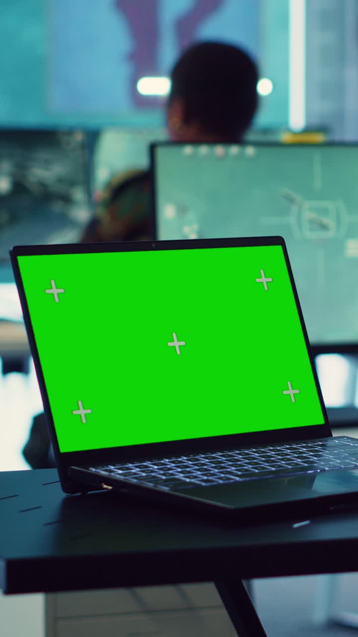 オフィスデスクにあるグリーンスクリーンのディスプレイが表示されたノートパソコン