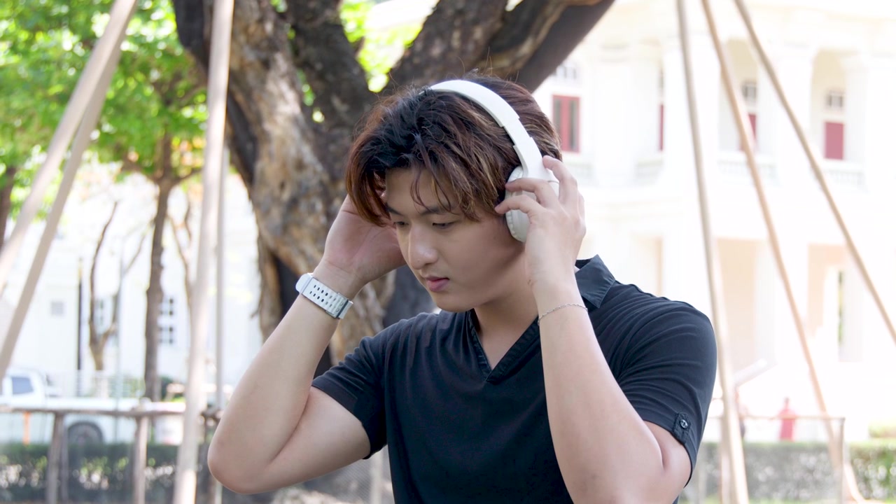 公園でヘッドホンをして音楽を聴く若いアジア人男性