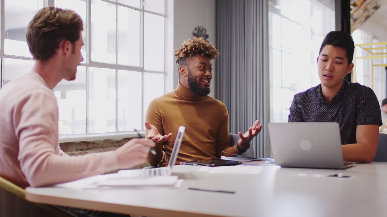 Young male creative business team working together in an office meeting room, close up, low angle