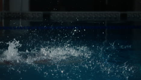 a swimmer in red swimming cap and goggles takes a dive in a pool.