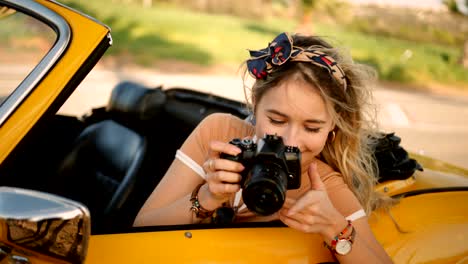 young woman in convertible car taking photos with camera