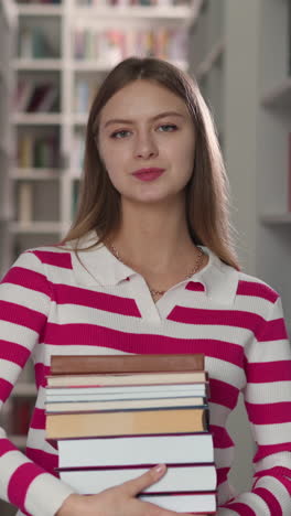 positive woman holds books standing in store aisle. blonde woman in casual clothes carries literature for homework in modern library. lady with detective novels