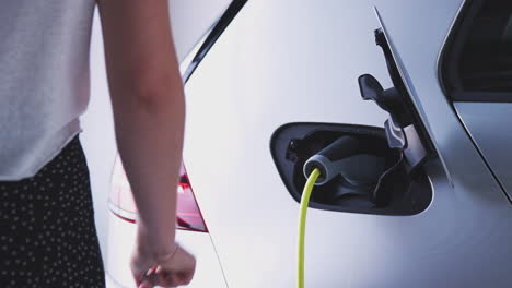 cerca de la mano conectando el cable de alimentación a un coche eléctrico ecológico de cero emisiones