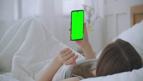 young woman lying in bed making a video call to the doctor looking at the green screen of the chromakey