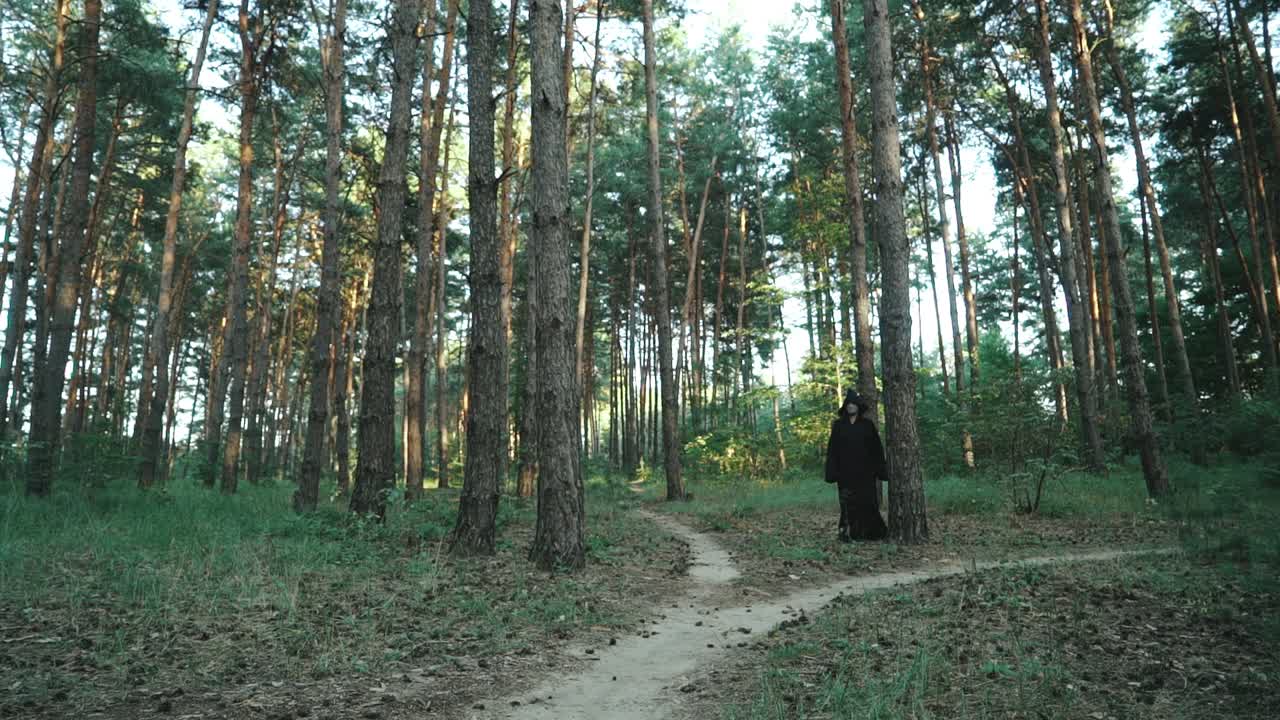 Evil witch hooded creature walking across forest. Halloween