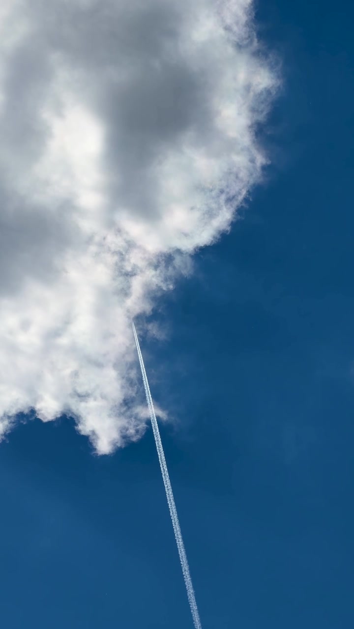 澄み切った青空を横切り、ふわふわした白い雲に向かって伸びる白い飛行機雲。