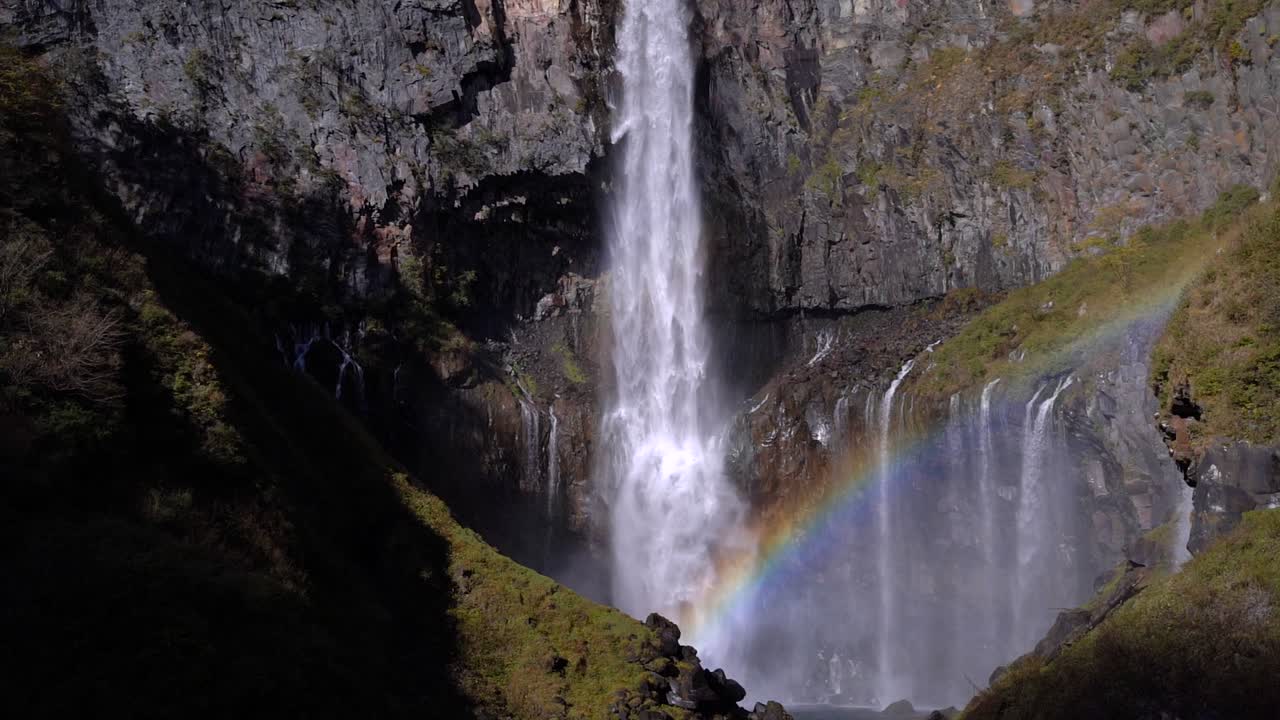 inclínate hacia abajo sobre una hermosa cascada alta que cae de las rocas con arco iris
