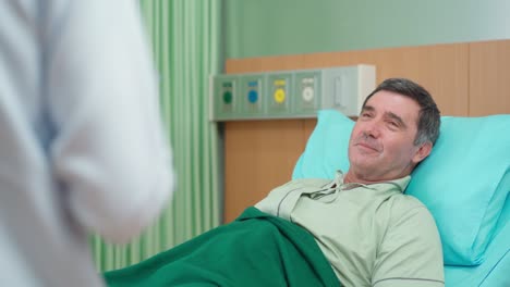 el médico y la enfermera en el abrigo de tierra visitan al anciano que se acuesta en la cama en la habitación del paciente en el hospital. el médico habla con el paciente y anima al paciente. el hombre se siente muy bien al volver a casa
