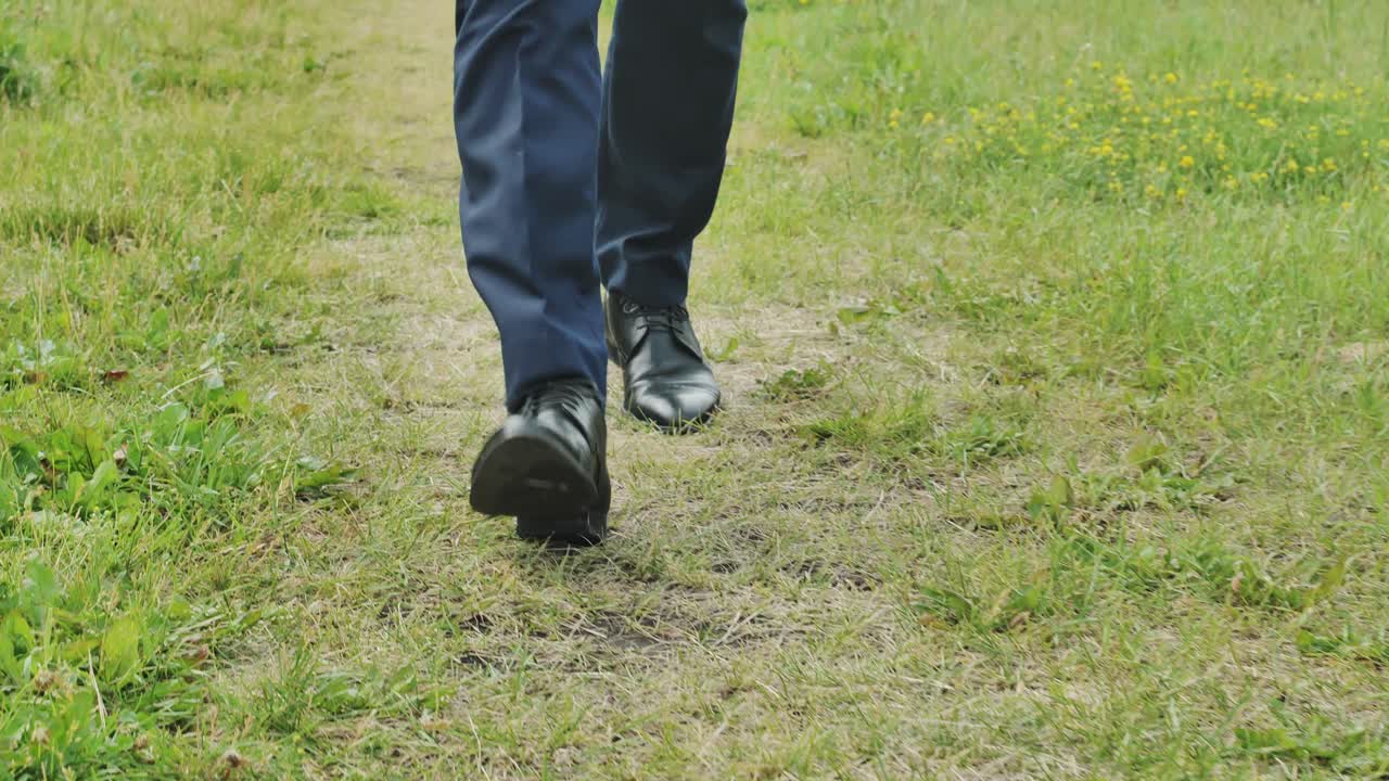 Homme élégant en chaussures de ville marchant le long d'un sentier naturel, la caméra reculant