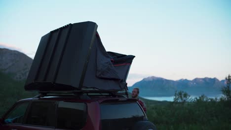 man setting up camping tent on top of the car