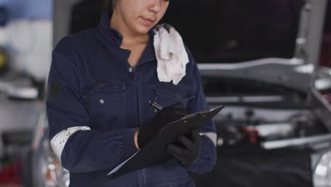 retrato de una mecánica tomando notas en el clipboard y sonriendo en una estación de servicio de automóviles