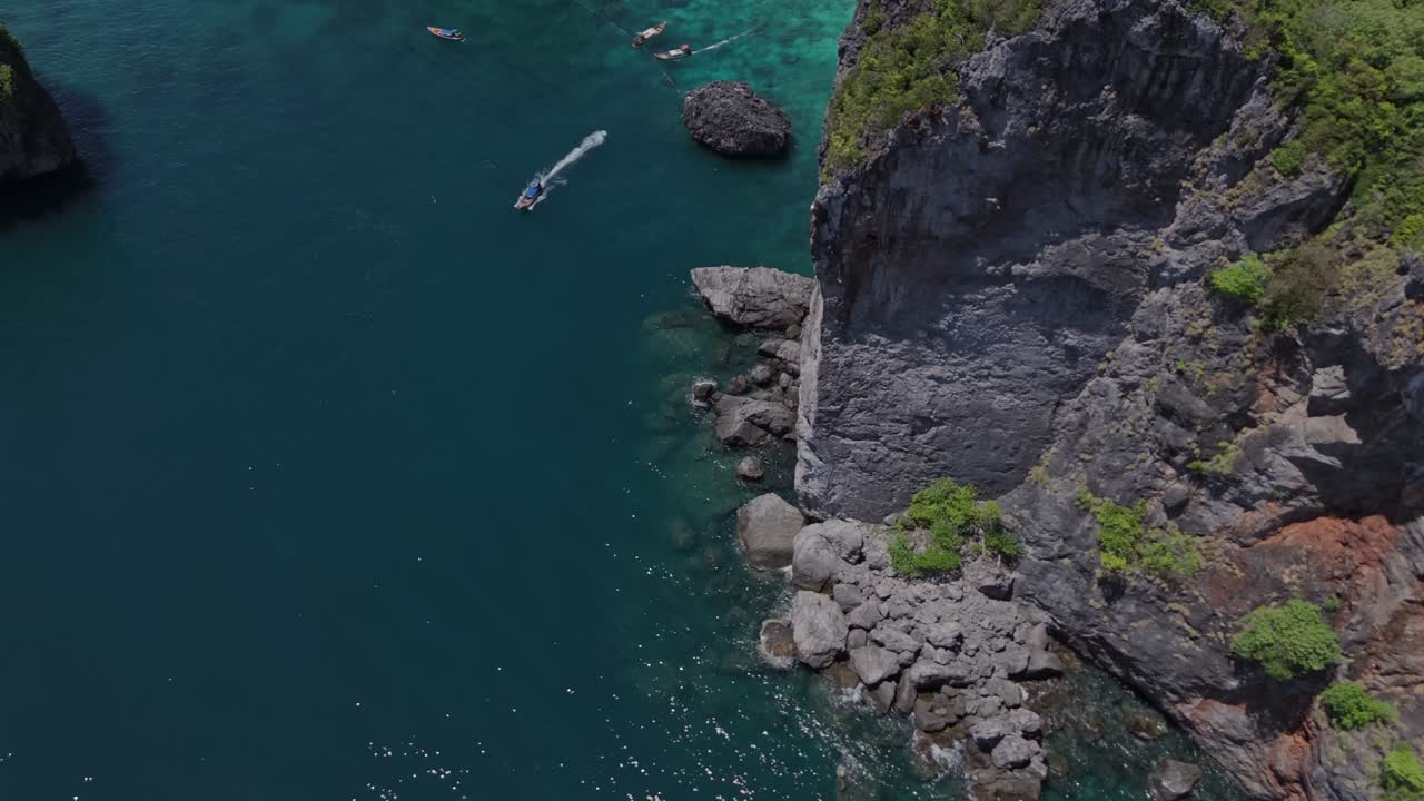 Drone flies forward while tilting up, revealing a hidden lagoon surrounded by limestone cliffs and tropical jungle in Phi Phi Islands, Thailand.