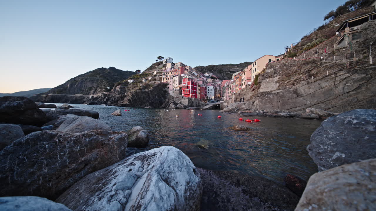 Colorful Riomaggiore coastline with clear water and rocky shore under the sunset light