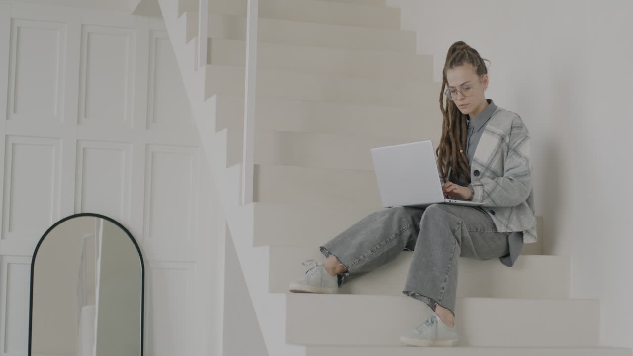 Woman working on laptop on stairs in a modern home