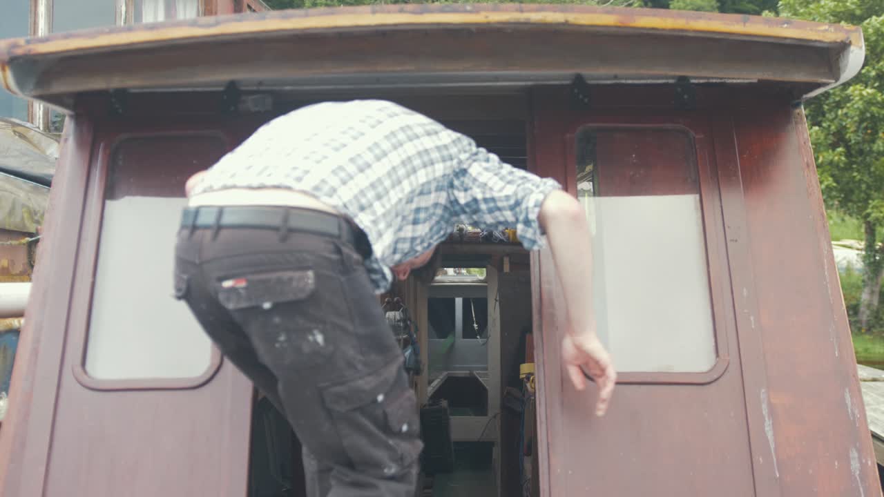 젊은 목수는 나무 보트 선실의 슬라이딩 도어를 열고 들어갑니다.