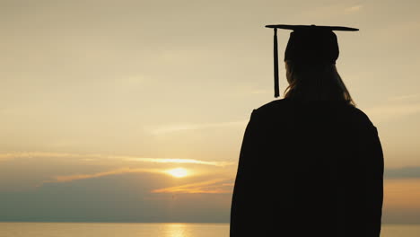 a bachelor with a diploma in hand and a cap of a graduate looks at the sunrise over the sea