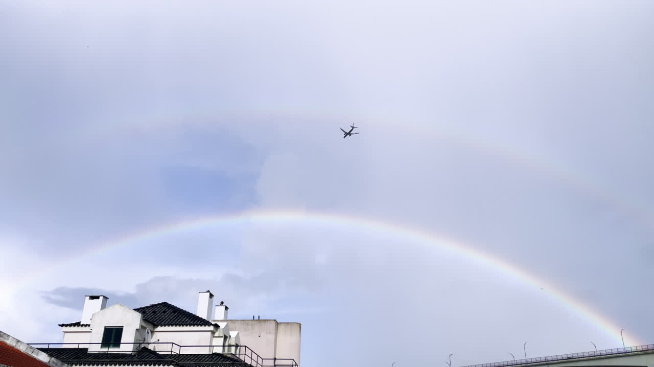 Plane coming in to land, flying through double rainbow above the famous 25th April Bridge in Lisbon, Portugal, Europe. Bird flying in the sky, natural phenomena