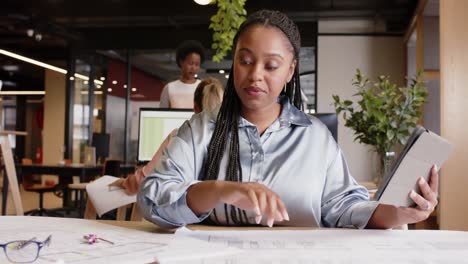 african american businesswoman sitting at desk and using tablet at office, in slow motion