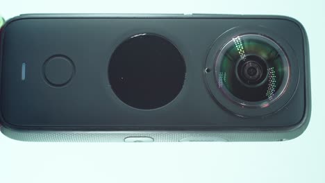 a close up vertical shot of a 360 camera with dual lens, two lens covers, shiny studio lighting reflecting, round screen, function button, on a rotating stand, slow motion, 4k video