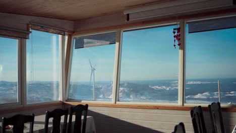 A-View-of-a-Windmill-Through-the-Glass-Window-of-Møllestua-During-the-Winter-Season-in-Bessaker,-Trondelag-County,-Norway---Handheld-Shot