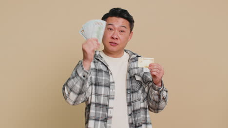 happy asian man showing plastic credit bank card and money dollar cash advertising taking loan